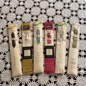 May include: Six packages of Talon zippers in various colors, including white, blue, pink, and beige. The packages are labeled with the Talon brand name and the type of zipper, such as "Neckline" and "Knit".