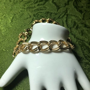 May include: A gold chain bracelet with a linked design. The bracelet is on a white hand model.