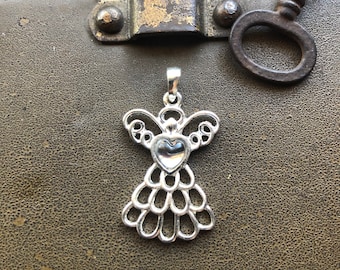 May include: Silver angel pendant with a heart in the center. The pendant is on a brown textured surface.