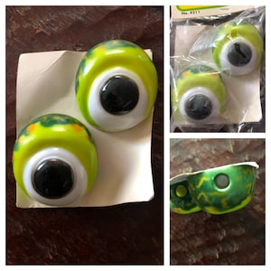 May include: A collection of large, plastic googly eyes with a bright yellow-green base, white iris, and black pupil. Some are loose, others are packaged. The eyes have green and orange accents. The packaging has the number 4211.