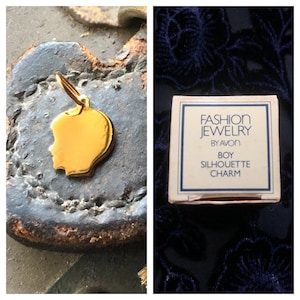May include: Gold-toned boy silhouette charm in its original box. The box is white with blue lettering that reads "Fashion Jewelry by Avon Boy Silhouette Charm".