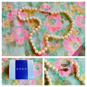 May include: A white pearl necklace with a gold clasp, displayed on a floral patterned fabric. The necklace is in a blue box with the word "AVON" printed on it.
