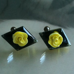 May include: Two diamond-shaped cabinet knobs with a black background and a yellow rose design.