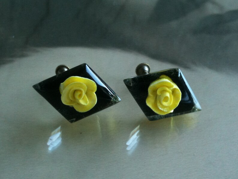 May include: Two diamond-shaped cabinet knobs with a black background and a yellow rose design.