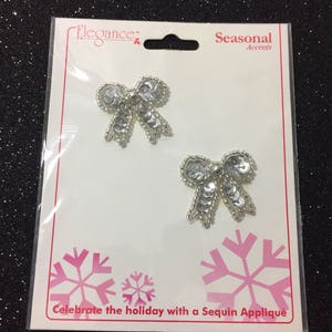 May include: Two silver sequin bows on a white card with the text "Elegance" and "Seasonal Accents". The card also says "Celebrate the holiday with a Sequin Appliqué".