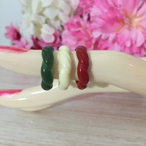 May include: Three twisted plastic rings in green, white, and red colors. The rings are stacked on top of each other.