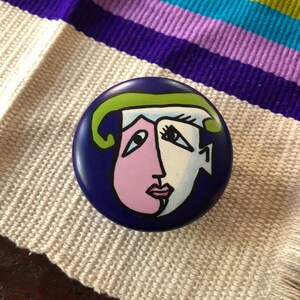 May include: A blue ceramic trinket box with a painted design of a face with green, pink, white, and black details. The box has a number "1" painted on the side.