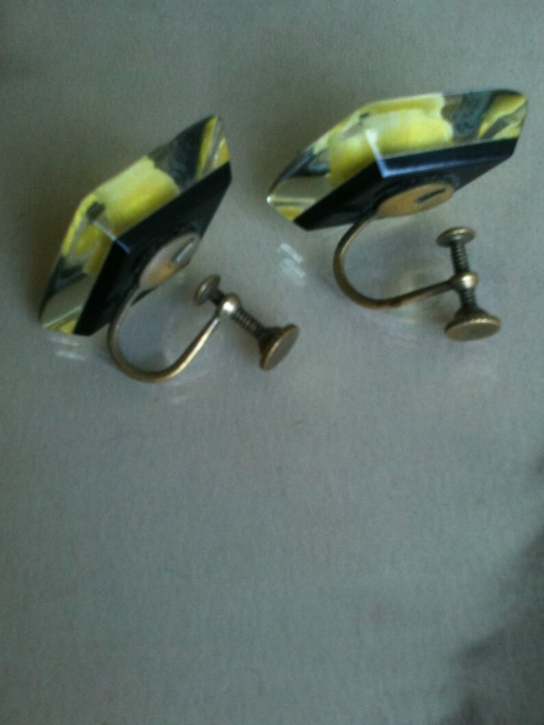 May include: A pair of yellow and black geometric clip-on earrings with gold metal backs.