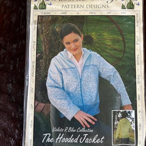May include: A pattern design package titled "Favorite Things" features a woman wearing a light blue hooded jacket with a floral pattern. The package includes the text "Violets R Blue Collection" and "The Hooded Jacket."