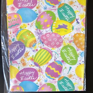 Pode incluir: Papel de embrulho branco com um padr&atilde;o de ovos de P&aacute;scoa coloridos. Os ovos s&atilde;o rosa, amarelo, azul e verde com listras brancas e amarelas. O papel tem as palavras "Happy Easter" escritas &agrave; m&atilde;o.