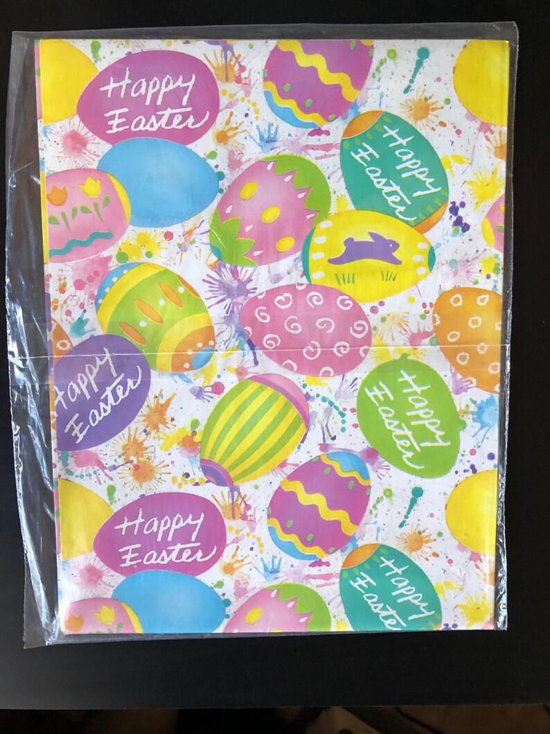 Pode incluir: Papel de embrulho branco com um padr&atilde;o de ovos de P&aacute;scoa coloridos. Os ovos s&atilde;o rosa, amarelo, azul e verde com listras brancas e amarelas. O papel tem as palavras "Happy Easter" escritas &agrave; m&atilde;o.