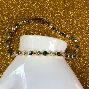 May include: A gold bracelet with alternating clear and green rhinestones.