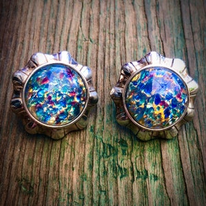 May include: A pair of silver tone earrings with iridescent blue, green, and gold glass cabochons. The cabochons have a speckled, textured surface.