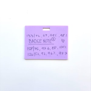Puede incluir: Una insignia rectangular de color morado claro con una ranura horizontal en la parte superior. La superficie presenta texto negro escrito a mano: "133/72, 67, 99%, 98.1", "BADGE NOTE", un s&iacute;mbolo de coraz&oacute;n, "158/76, 97.6, 88, 100%" y "126/52, 92, 96%, 97.7" en tres filas.