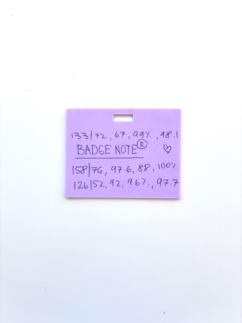 Puede incluir: Una insignia rectangular de color morado claro con una ranura horizontal en la parte superior. La superficie presenta texto negro escrito a mano: "133/72, 67, 99%, 98.1", "BADGE NOTE", un s&iacute;mbolo de coraz&oacute;n, "158/76, 97.6, 88, 100%" y "126/52, 92, 96%, 97.7" en tres filas.