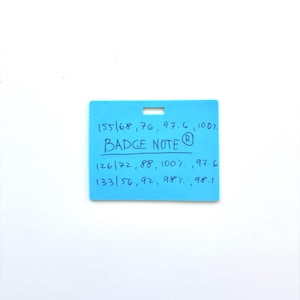 Puede incluir: Una insignia rectangular de pl&aacute;stico azul claro con una ranura en la parte superior central. La insignia presenta un texto manuscrito en azul oscuro que dice: 155/68, 76, 97.6, 100%, BADGE NOTE, 126/72, 88, 100%, 97.6, 133/56, 92, 98%, 98.1, con un s&iacute;mbolo de marca registrada.