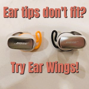 May include: Two wireless earbuds with the Bose logo, one with an orange ear wing and the other with a black ear wing. The text "Ear tips don't fit? Try Ear Wings!" is displayed above and below the earbuds.