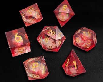 May include: A collection of seven red resin dice with gold numerals. Each die features a glittery, iridescent core. The dice are in various geometric forms, including a cube, a tetrahedron, and a 20-sided die. Ideal for tabletop gaming.