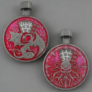 May include: Two silver and red dice rollers with a dragon and Cthulhu design. Each roller has a number display and a handle. The dragon roller shows numbers 17, 3, 10, 4, and 3. The Cthulhu roller shows numbers 3, 5, and 4.