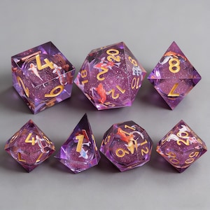 May include: Set of seven polyhedral dice with a purple, glittery interior. Each die features gold numbering and miniature koi fish. The dice are designed for tabletop role-playing games.