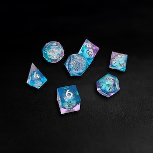 May include: A collection of seven iridescent polyhedral dice in blue, purple, and clear. Each die features white numbering. The dice are displayed on a black surface, with shapes including a d20, d12, d10, d8, d6, d4, and a d10 percentile.