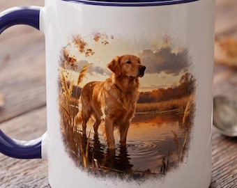 Könnte beinhalten: Ein weißer Keramikbecher mit dunkelblauem Innenraum und Henkel, bedruckt mit einer Illustration eines Golden Retrievers, der bei Sonnenuntergang in flachem Wasser steht, umgeben von hohem Gras und einem Himmel in warmen Orange- und Brauntönen.