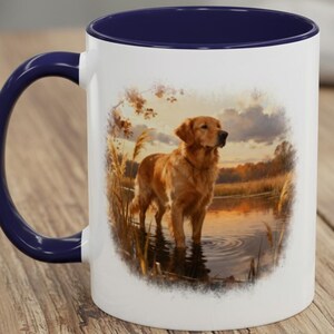 May include: White ceramic mug with a navy blue interior and handle. The mug features a detailed illustration of a golden retriever standing in water at sunset. The dog is a light brown color, and the background includes reeds and a lake.