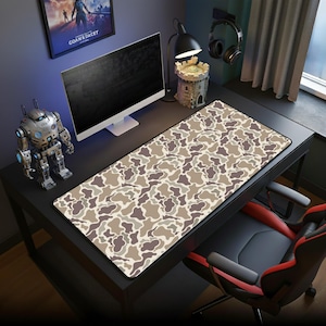 May include: A rectangular desk mat with a camouflage pattern in shades of brown, tan, and gray. The mat is placed on a black desk, with a computer monitor, robot figurine, and other accessories visible in the background.