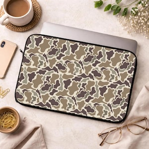 May include: A laptop sleeve with a camouflage pattern in shades of brown, tan, and olive green. The sleeve has a black border and a zipper closure. The design is reminiscent of military or outdoor gear.