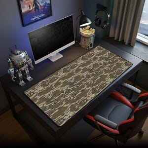 May include: A large rectangular mouse pad with a camouflage pattern in shades of brown, tan, and gray. The pad is on a black desk, with a computer monitor, robot figurine, and other accessories.