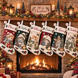 Könnte beinhalten: Sechs Weihnachtsstrümpfe hängen in einer Reihe, jeder mit einer Kätzchen-Illustration, einer weißen Manschette mit Namen und Stechpalmen-Akzenten. Die Strümpfe sind rot, grün und cremefarben, mit Schneeflocken und Geschenken verziert.