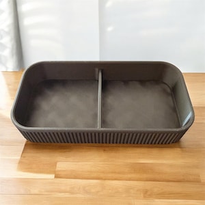 May include: A rectangular, dark brown storage bin with a divider, ideal for organizing items. The bin has a textured interior and a ribbed exterior design. The bin is sitting on a wooden surface.