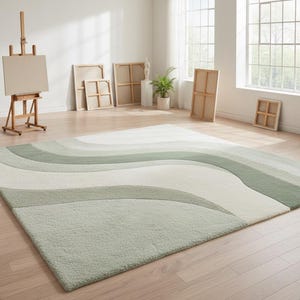 Peut inclure: Un grand tapis rectangulaire avec un motif ondulé dans des tons de vert et de blanc. Le tapis est posé sur un parquet dans une pièce lumineuse, avec des fournitures d'art et des toiles en arrière-plan. Les dimensions du tapis ne sont pas visibles.