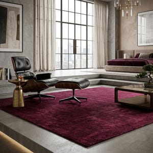 Puede incluir: Una alfombra rectangular grande de color burdeos intenso con un pelo texturizado y suave. La alfombra está colocada sobre un suelo de hormigón en una habitación que cuenta con un sillón de cuero negro con reposapiés a juego y mesa de centro.