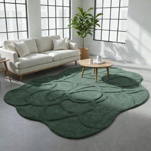 May include: A green, leaf-shaped area rug with a textured, raised pattern. The rug is in a living room setting with a white sofa, wooden coffee table, and large windows. The rug's unique design adds a touch of nature to the room.