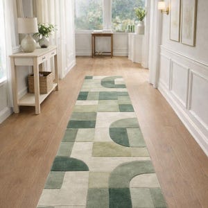 May include: A long, rectangular rug with a geometric pattern in shades of green and cream. The rug is placed in a hallway with light-colored walls and hardwood floors. The design features squares and curved shapes.
