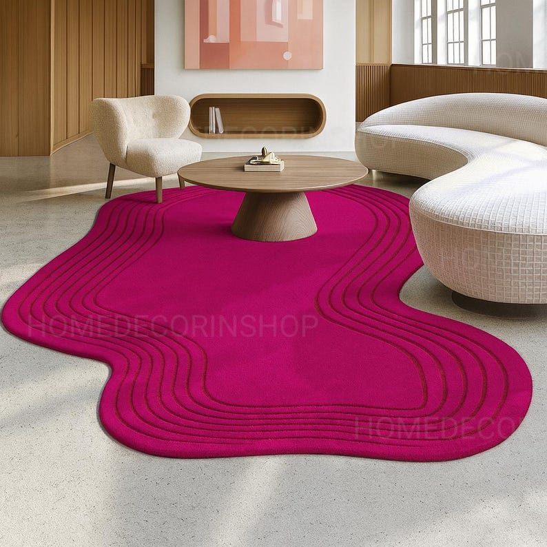 Op de afbeelding: Een levendig fuchsia tapijt met een unieke, organische vorm en een gelaagd, golvend ontwerp. Het tapijt is het middelpunt van een moderne woonruimte en vormt een aanvulling op de neutrale meubels en inrichting. De tekst "HOMEDECORINSHOP" is zichtbaar op het tapijt.