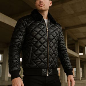 May include: Black quilted bomber jacket with a faux fur collar and a gold zipper. The jacket has a diamond pattern and ribbed cuffs. The model is wearing black pants and a white t-shirt.