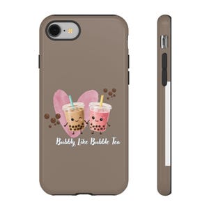 May include: A brown phone case featuring a watercolor heart and two cartoon bubble tea drinks. The drinks have smiling faces and are holding hands. The text "Bubbly Like Bubble Tea" is below the drinks.