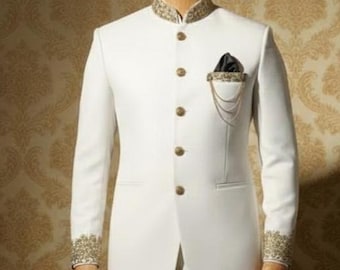 May include: A white suit with a mandarin collar, gold buttons, and gold embroidery on the collar and cuffs. A black pocket square with a gold chain adds detail. The suit is displayed on a mannequin.