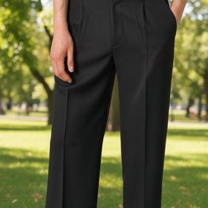 Op de afbeelding: Zwarte broek met een geplooid voorpand. De broek heeft een rechte pijp en wordt gedragen met witte schoenen. De persoon staat op groen gras in een park.