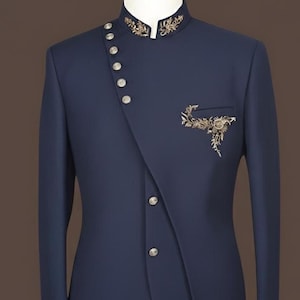May include: A navy blue suit jacket with a mandarin collar and an asymmetrical button closure. The jacket has gold embroidery on the collar and pocket. It is displayed on a mannequin.