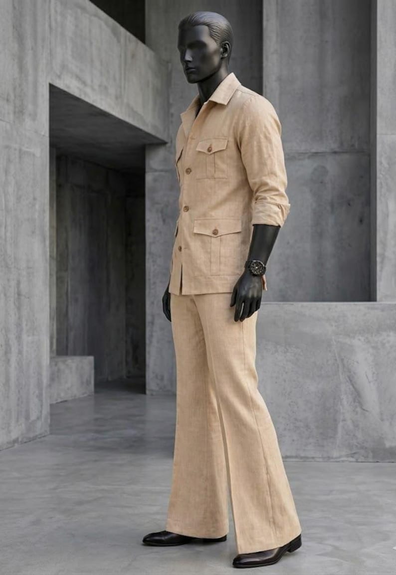 May include: A tan linen suit on a mannequin. The suit includes a collared jacket with four pockets and matching flared pants. The mannequin wears a black watch and black gloves. The suit is a neutral color and has a classic design.