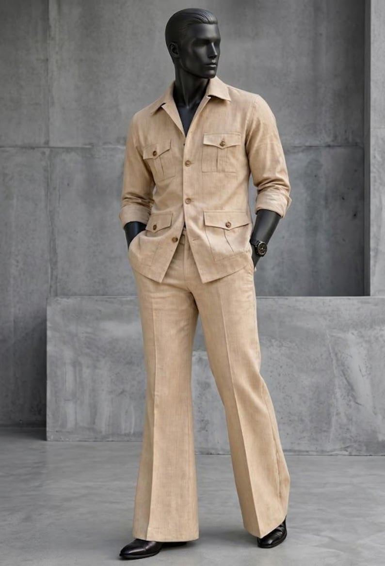 May include: A tan linen suit on a mannequin. The suit includes a long-sleeved jacket with four front pockets and matching flared trousers. The mannequin wears a black watch and black shoes. The background is a gray concrete wall.