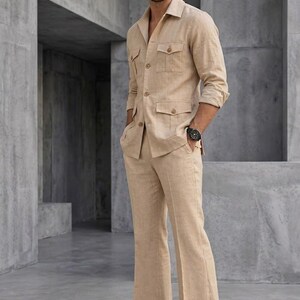 May include: A tan linen suit featuring a collared jacket with four front pockets and matching flared trousers. The jacket has long sleeves and the trousers have a wide leg. The suit is paired with black dress shoes and a black watch.
