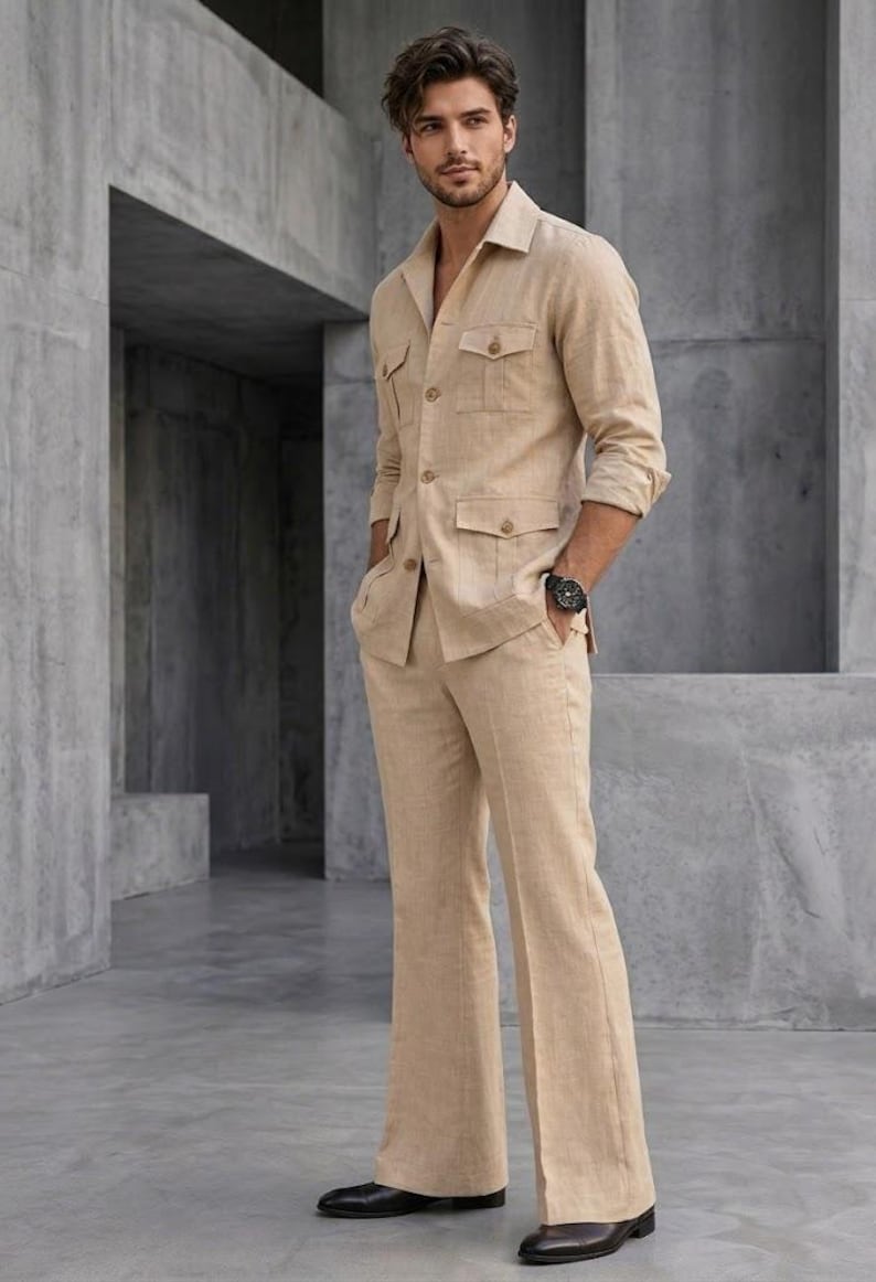 May include: A tan linen suit featuring a collared jacket with four front pockets and matching flared trousers. The jacket has long sleeves and the trousers have a wide leg. The suit is paired with black dress shoes and a black watch.