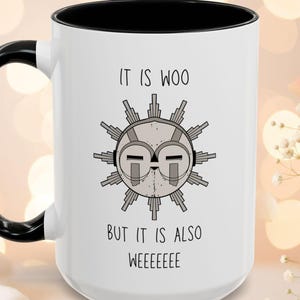 May include: White ceramic mug with a black interior and handle. The mug features a graphic of a sun-like face with the text "IT IS WOO BUT IT IS ALSO WEEEEEEE".
