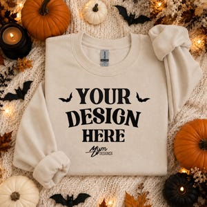 Könnte beinhalten: Ein cremefarbenes Sweatshirt mit Rundhalsausschnitt und dem schwarzen Schriftzug "YOUR DESIGN HERE" mittig auf der Brust, flankiert von zwei kleinen schwarzen Fledermaussilhouetten, mit dem Text "MYM DESIGNSX" in kleinerer Schrift darunter.