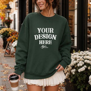 Könnte beinhalten: Ein dunkelwaldgrünes Sweatshirt mit Rundhalsausschnitt und dem weißen Schriftzug "YOUR DESIGN HERE" in einer fetten Serifenschrift auf der Brust, wobei sich das kleinere weiße Logo "Mym DESIGNSX" direkt unter dem Haupttext befindet.