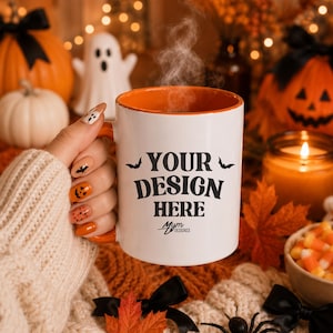 May include: A white ceramic mug with an orange interior and handle, featuring the black text "YOUR DESIGN HERE" flanked by two small black bat silhouettes, with a small "Mym Designsx" logo printed below the main text on the front surface.